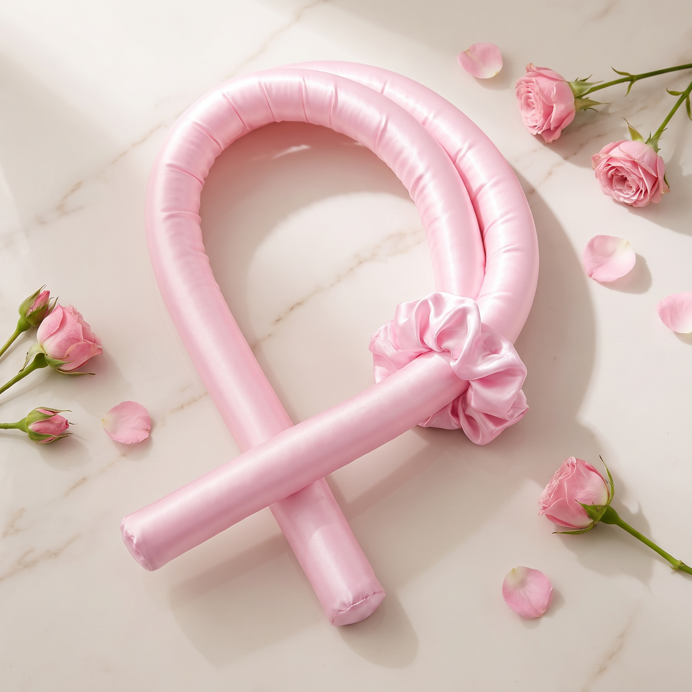 Revonae heatless curling rod coiled with satin scrunchie and pink roses on marble